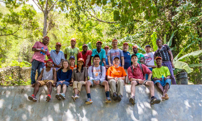 A diverse group of Clemson students sit on a wall with a group of international workers on a service trip in South America.