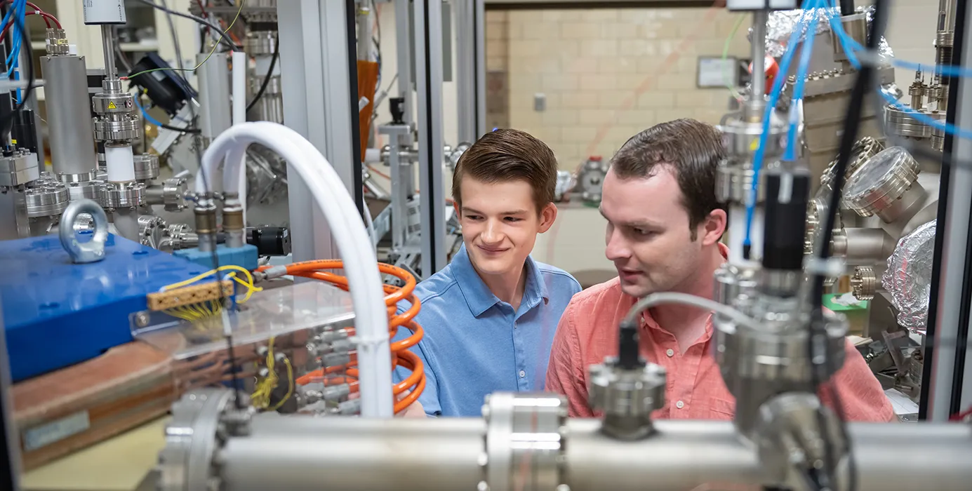 A male professor and a male student examine a large metallic machine.