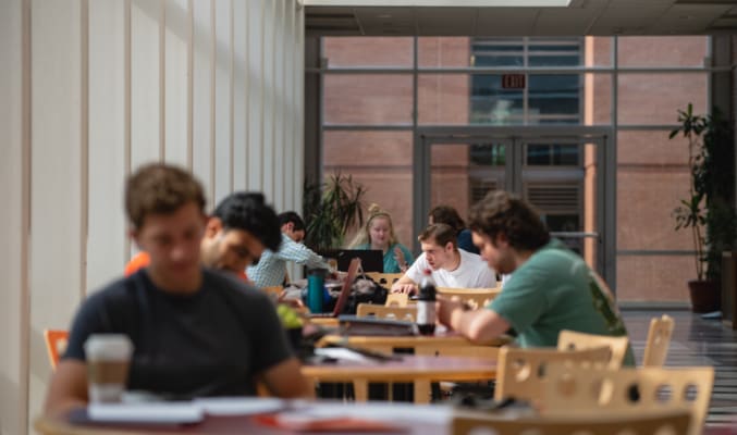 Clemson students study at tables in a window-lined corridor.
