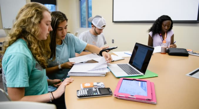 Three female students and one male student study together at a round table in the Academic Success Center.