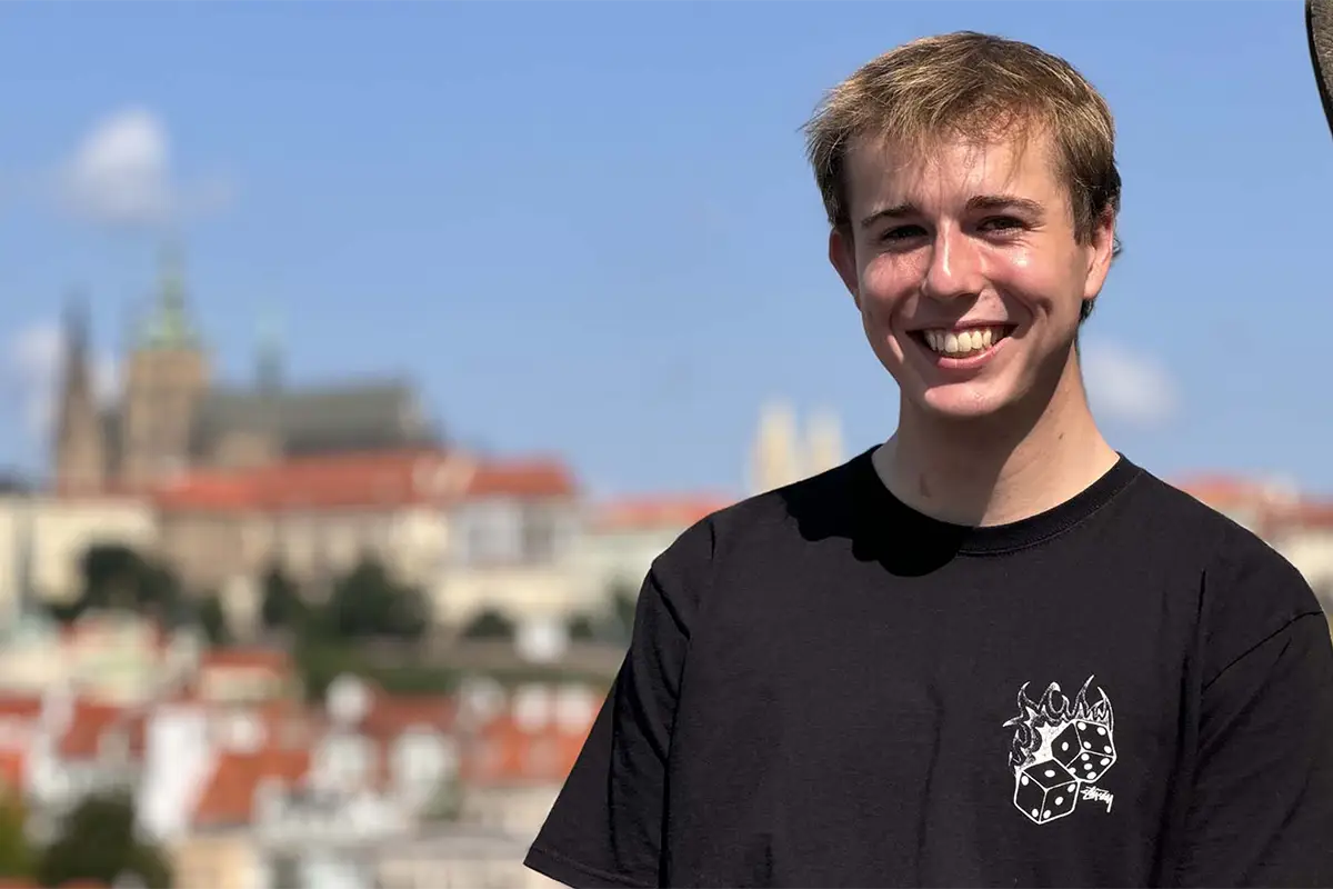 A male student wearing a black T-shirt poses in front of an out-of-focus cityscape during a study abroad trip.