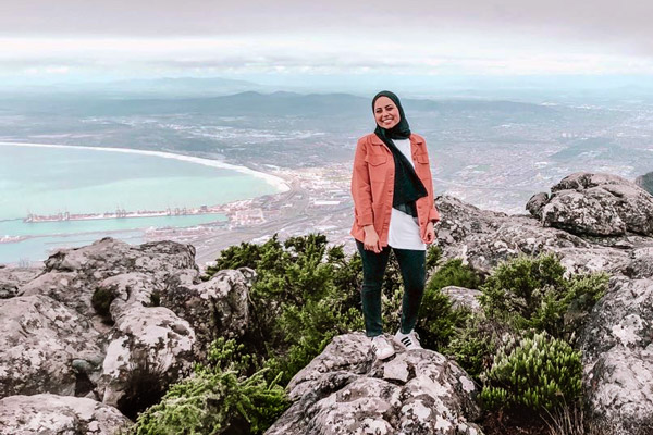 Student Roann Abdeladl stands atop Table Mountain in South Africa during a study abroad trip. In the far background is the ocean and the city of Cape Town.