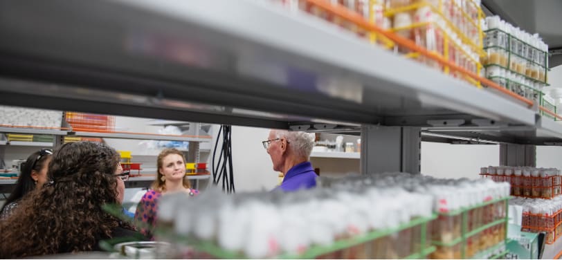 Medical researchers discuss a concept in the lab with bottles lining the shelves.