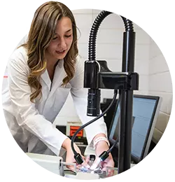 A female student wearing a white lab coat works with an imaging device.