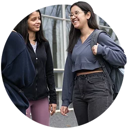 Three female students stand in a circle facing each other as they laugh in conversation.