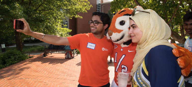 Two intenrational students take a selfie with the Clemson Tiger mascot on campus.