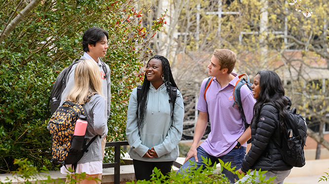Four students laugh next to the trees outside of Bracket Hall.