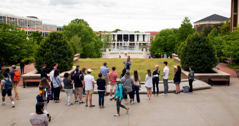 Student tour guide addresses her tour group while standing in front of Clemson's academic buildings.