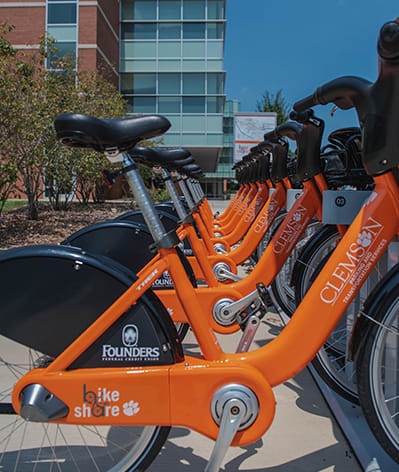 Orange bike-share bikes stand in a row outside Clemson's student center.