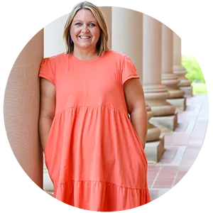 A female University employee wearing an orange dress poses by one of the large columns in front of Sikes Hall on campus.