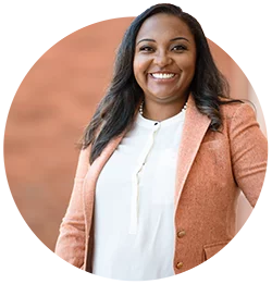 A female staff member wearing a white top and orange blazer poses for a portrait photo.