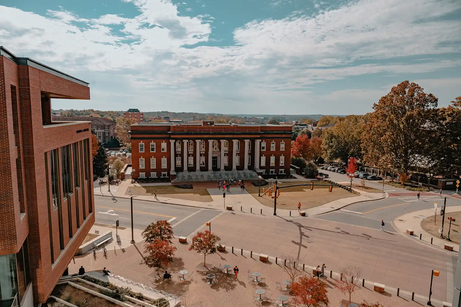 Elevated view of Sikes Hall with its white columns, overlooking a street and plaza surrounded by autumn trees.