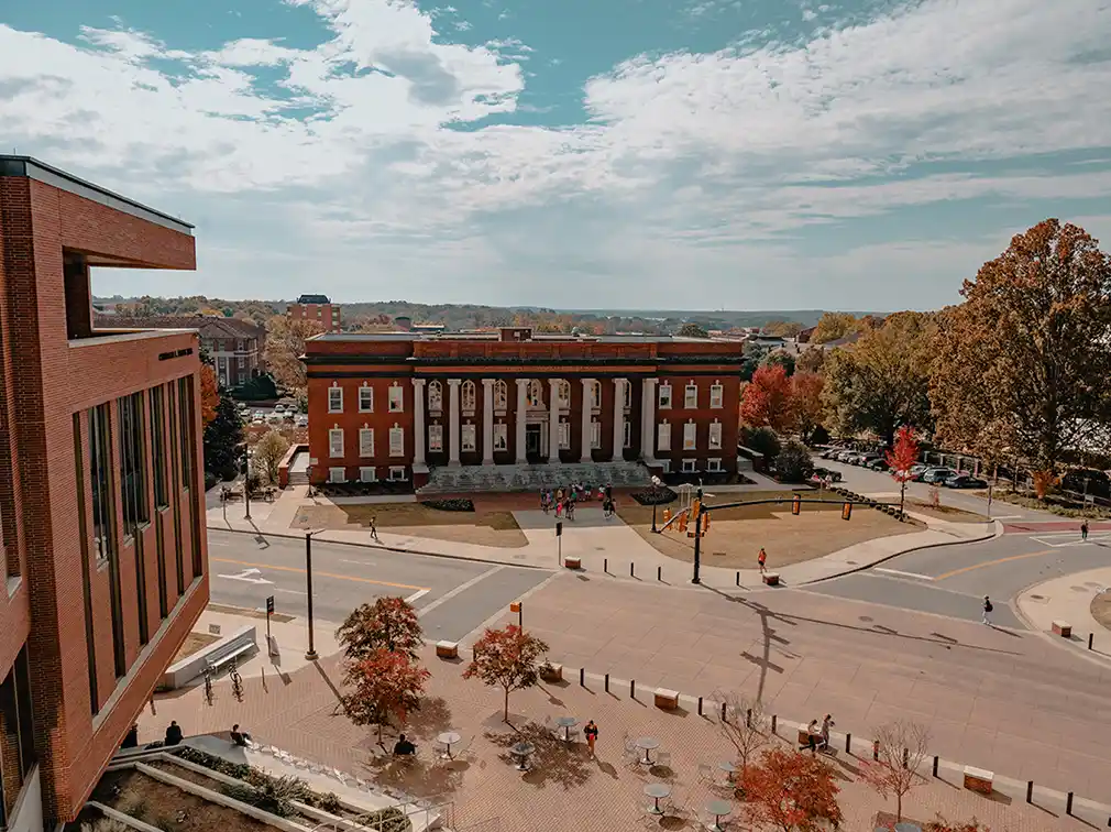 Elevated view of Sikes Hall with its white columns, overlooking a street and plaza surrounded by autumn trees.