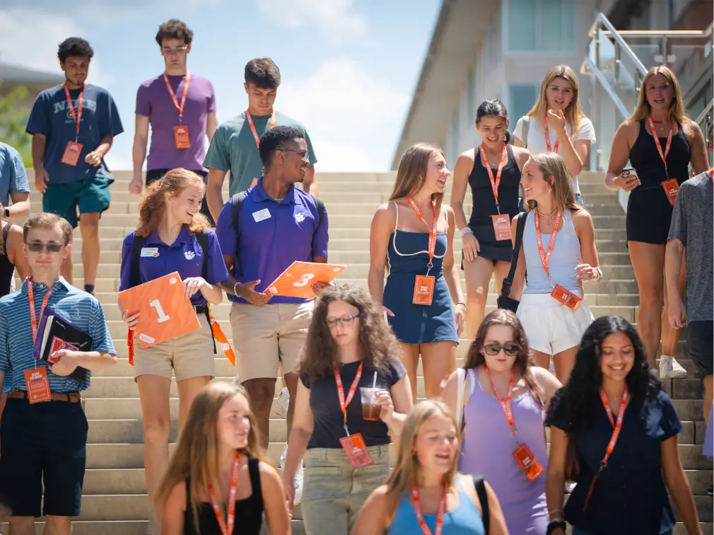 A crowd of first-year students wearing orange lanyards descend a set of stairs while attending orientation