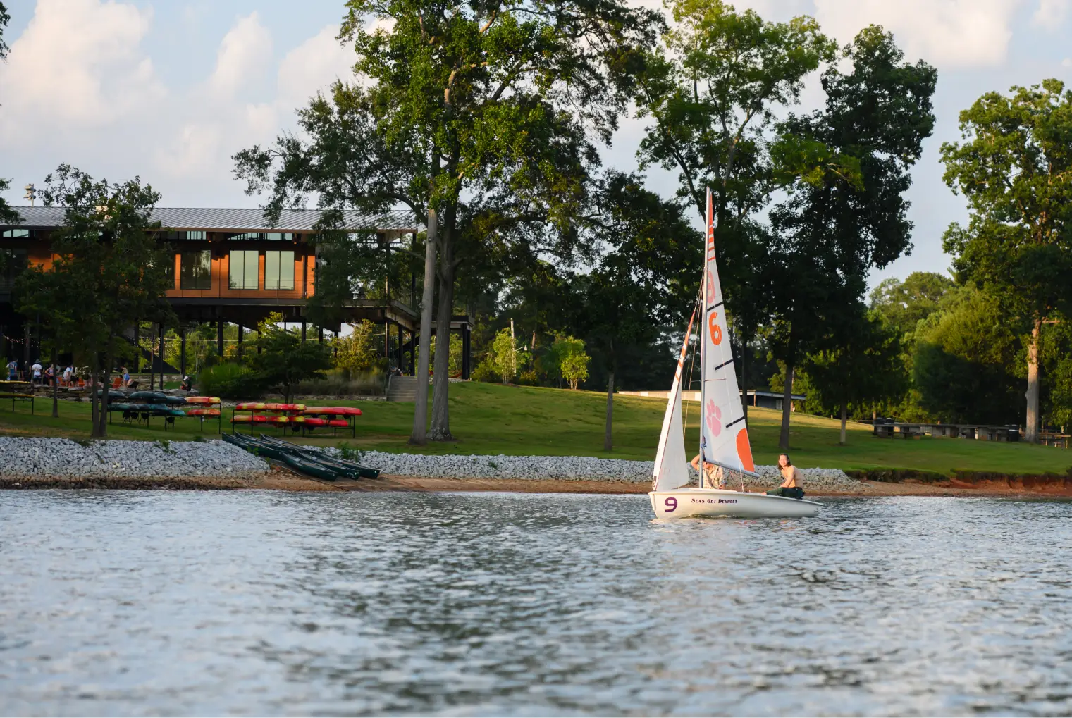 A female student pilots a small Clemson branded sailboat on Lake Hartwell in front of the Andy Quattlebaum Outdoor Center