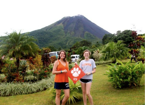 Caitlin and friend hold a tiger rag while standing in front of a large mountain.