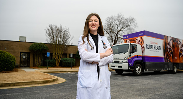 Caitlin Kickham stands smiling in front of the Clemson Rural Health Mobile Clinic.