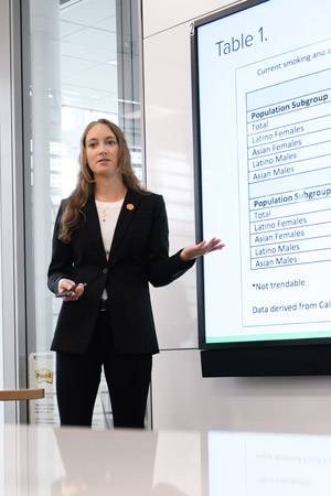 Emily Martin presents her research findings in a bright window-lined room wearing a black suit and orange Tiger Paw pin.