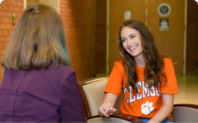 Emily Martin smiles and talks with her female professor in a brick-walled campus building.