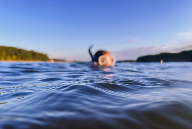 A blurred photo of a masked swimmer wearing a snorkel whose head is just above water.