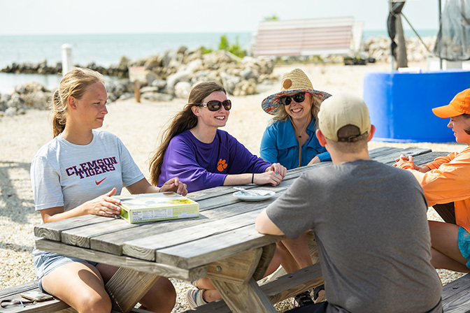A group of students sits at a picnic table eating Key Lime Pie on the beach. 