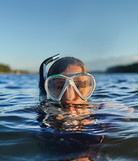 A close-up headshot of undergraduate biological sciences student Erin Griffin who looks at the camera wearing a snorkel and mask with her head just above the waterline where she is floating.