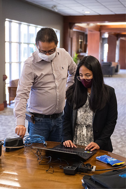 Joe assists a colleague as they work on a computer.