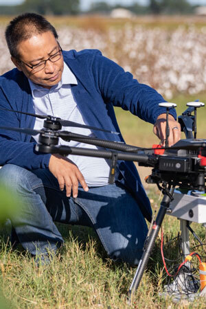 Joe crouches down to investigate a drone as it rests in the grass.