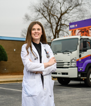 Caitlin Kickham poses in a white coat in front of the Clemson Rural Health mobile health unit