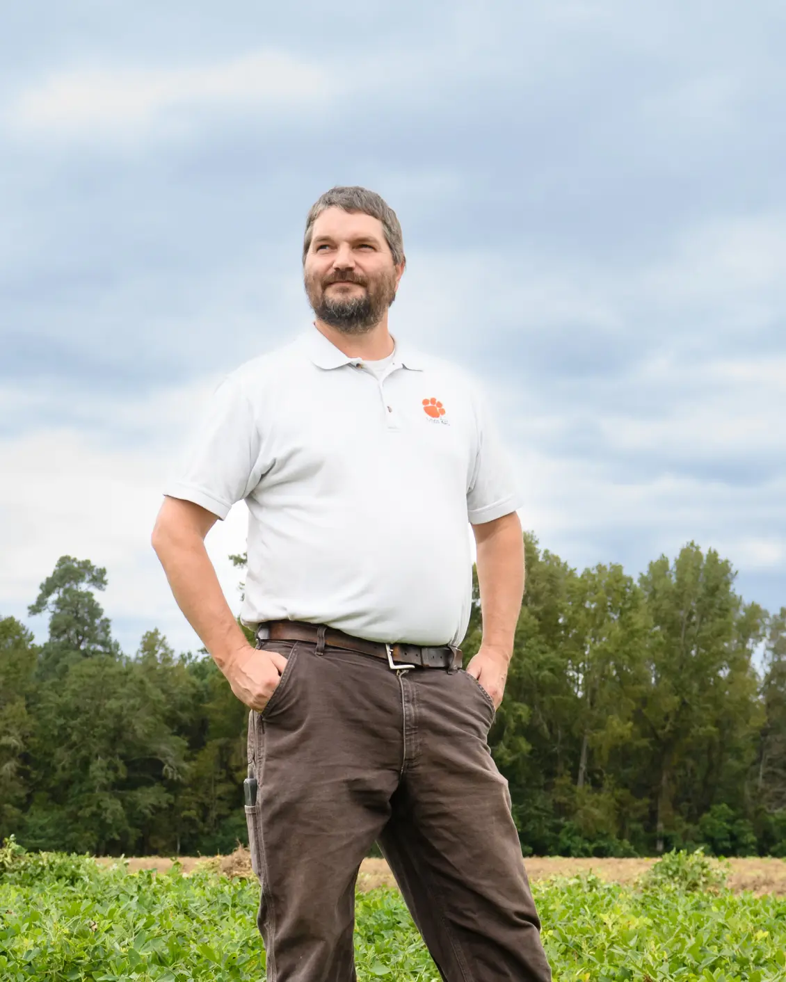 Kendall Kirk stands in front of a field of crops with a treeline in the background.