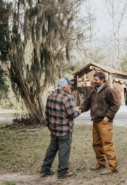 Kendall Kirk shakes hands with a farmer with a house in the background.