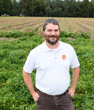 Kendall Kirk poses in front of a feild of peanuts at the Edisto Research Center