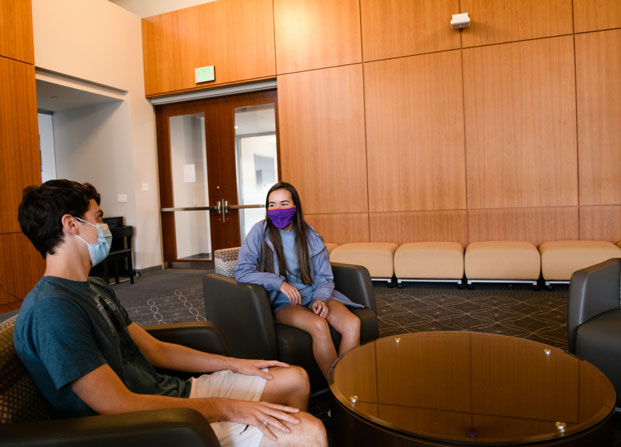 Marena is sitting and having a conversation with another student inside a meeting space on campus.