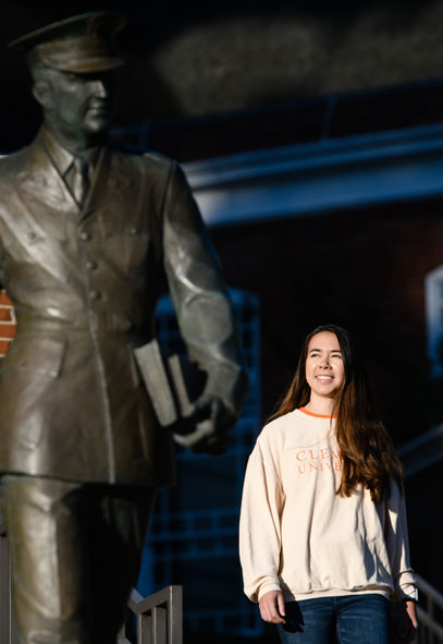 Marena is posing in front of a statue of a man who is dressed in military uniform carrying books.