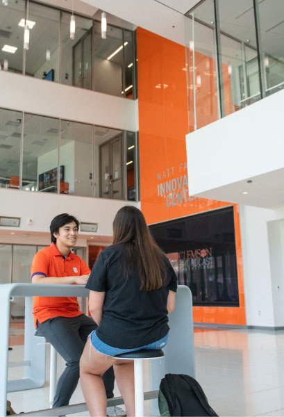 Nam sits and talks with a female friend at a table in the lobby of Watt Innovation Center.