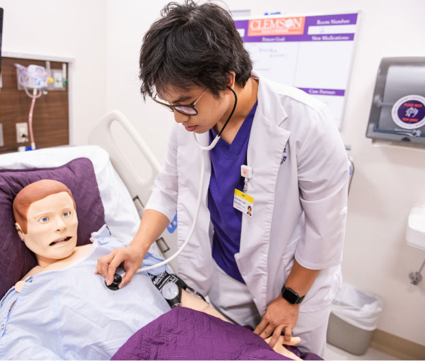 Nam uses a stethoscope to listen to the heartbeat of a human simulator in the Clemson nursing lab.