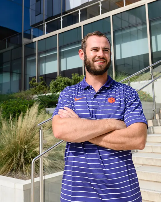 Hunter Renfrow standing in front of the the steps of the Clemson College of Business with his arms folded.