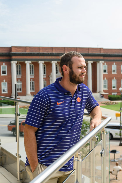 Hunter is leaning against a railing with his left arm while looking off to the right of the camera with Sikes Hall being visible in the background.