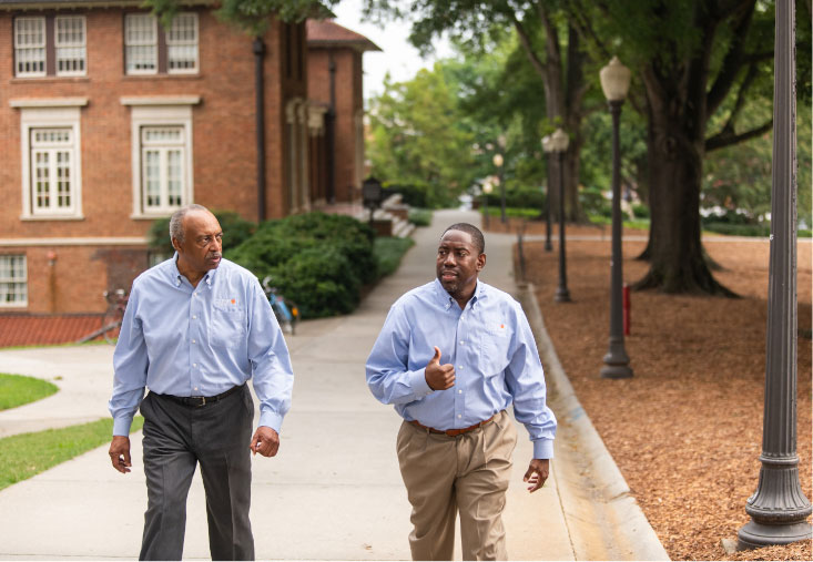 Roy walks along the sidewalk in front of Holtzendorff Hall talking with his Call Me MISTER® colleague, Mark.