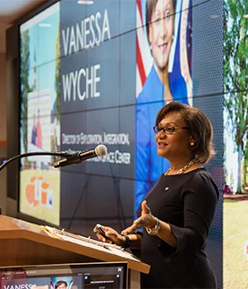 Vanessa stands at a lecturn giving a presentation to students