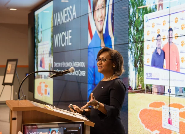 Vanessa speaks at a podium in front of a video board displaying her name and title