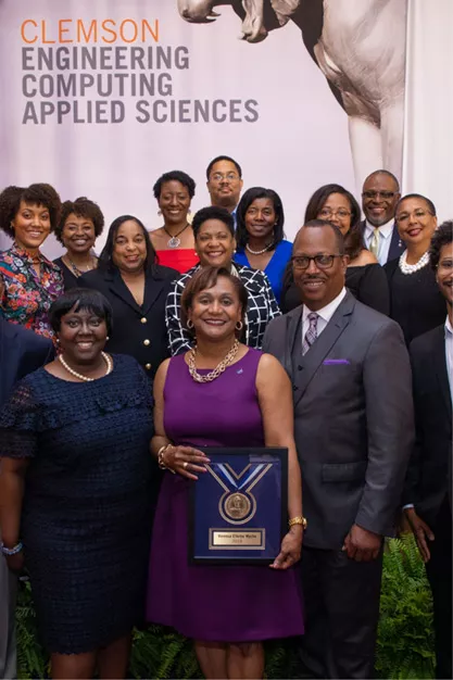 Vanessa poses with a group holding her Clemson Hall of Fame plaque in front of a sign that reads Clemson Engineering Computing Applied Sciences