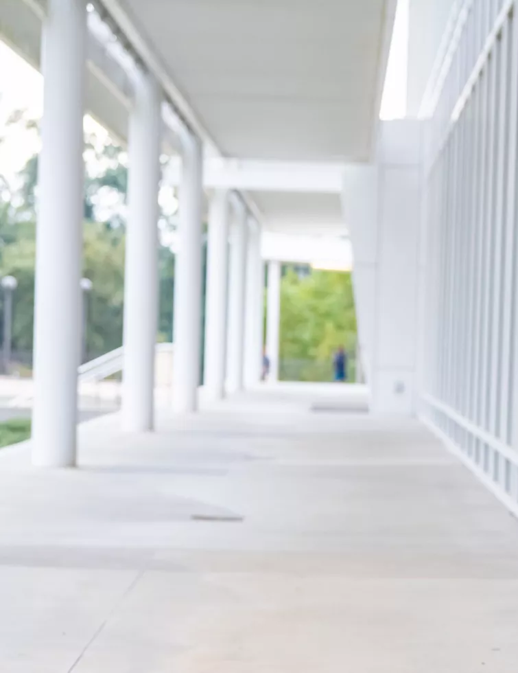 Vanessa smiles, standing with hands clasped in front of a bank of windows on Clemson's campus.