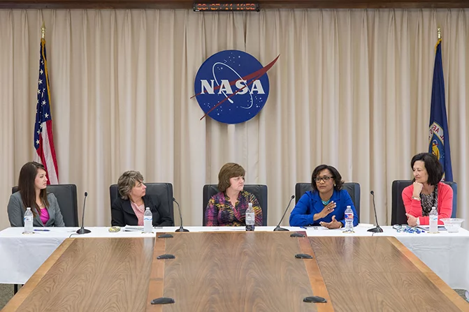 Vanessa speaks while seated at a table with four other women in front of a NASA sign