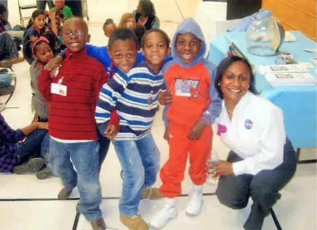 Vanessa kneels next to a group of young, smiling schoolchildren