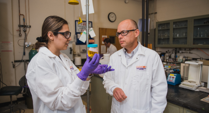 Two faculty members in a lab discuss a liquid sample.