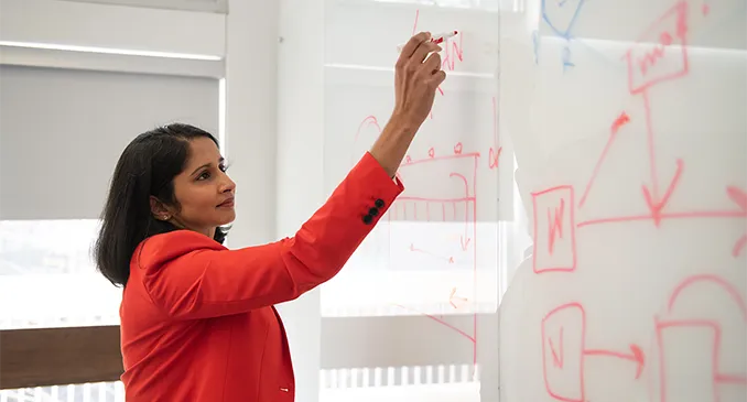 A female faculty member writes out and solves a problem on a classroom whiteboard
