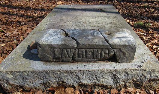 A grave ledger with inscriptions topped with a footmarker with Lawrence etched in the side.