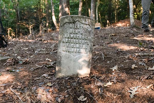 A single antiquated headstone in the woods.