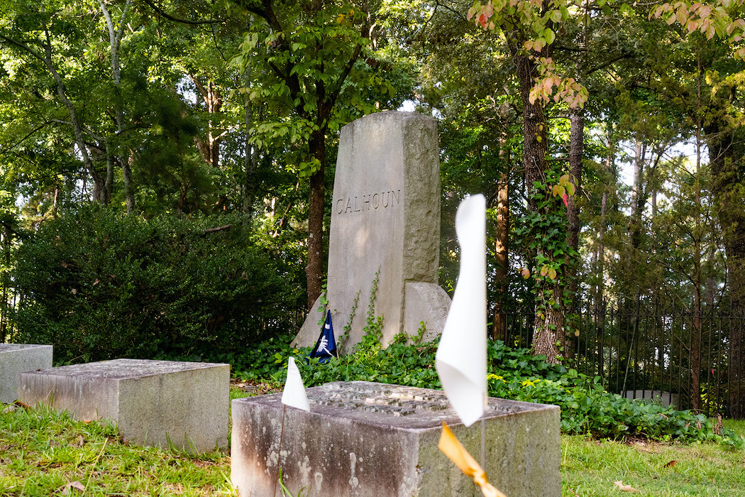 Graves for members of the Calhoun family are in front of a stone memorial with the inscription "Calhoun." A white flag denoting an unmarked grave is in the foreground, out of focus.